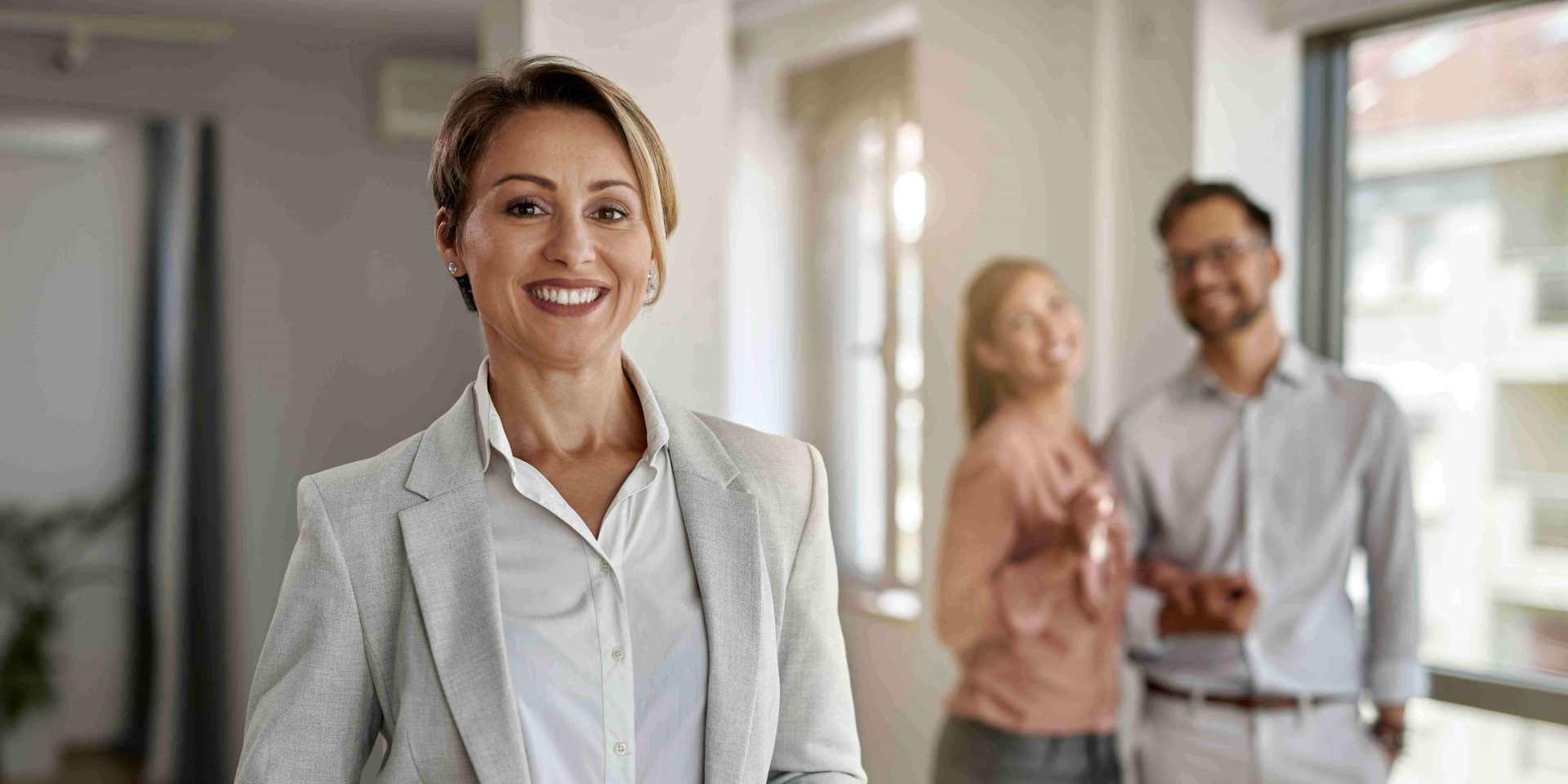 Female real estate agent standing in a house with a couple smiling behind her